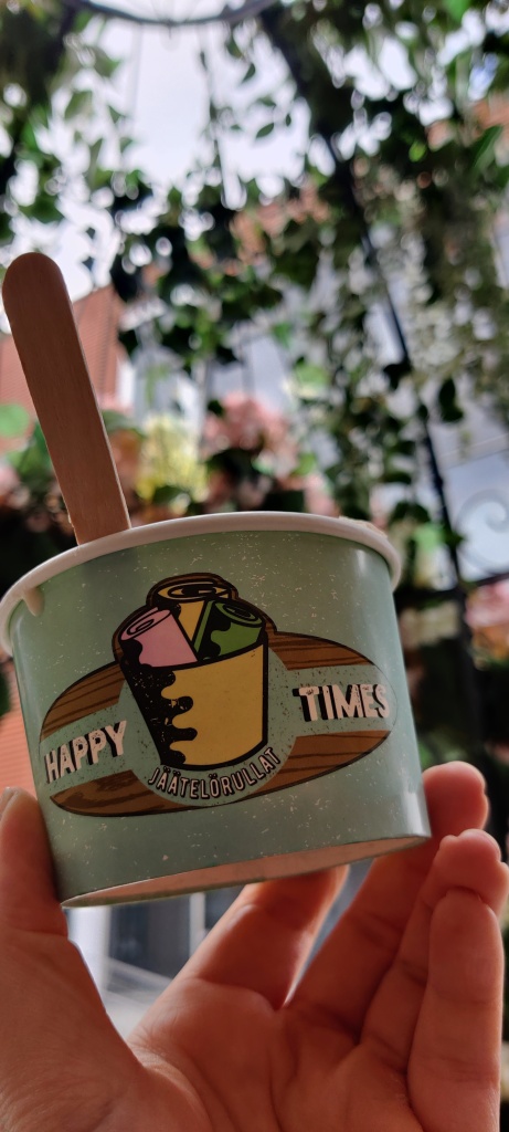 Lähikuva pahvisesta jäätelökulhosta, jossa lukee Happy Times jäätelörullat. Tausta on sumea, mutta kuva on otettu lintuhäkin sisällä istuessa.